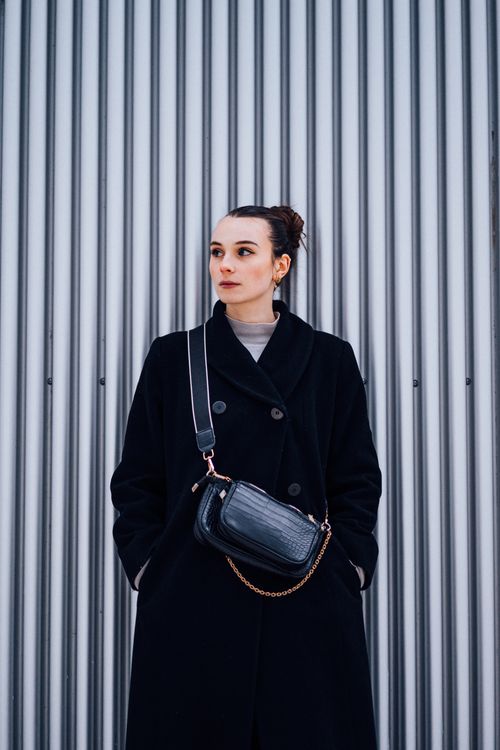 Free Stylish woman in a black coat standing against a corrugated metal wall in Namur, Belgium. Stock Photo