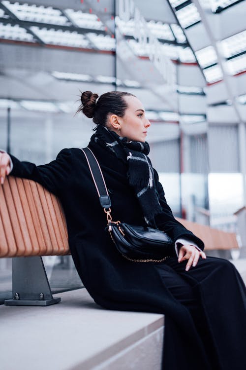 Woman in a Black Coat Sitting on a Bench 