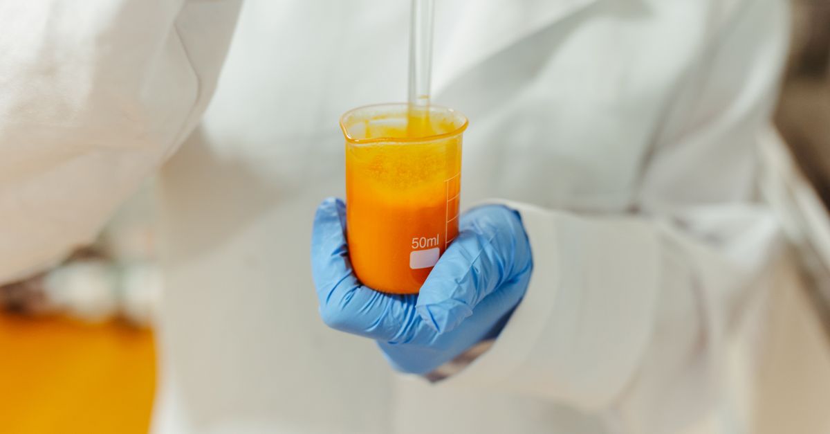 Close-up of a scientist in a lab coat holding a beaker with orange liquid using blue gloves. - Evidence evidence guide for carotenoid skin health meta-analysis