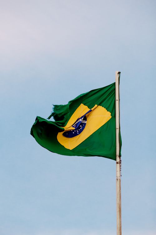 Free A Brazilian flag attached to a flagpole waving against a clear blue sky, symbolizing patriotism. Stock Photo