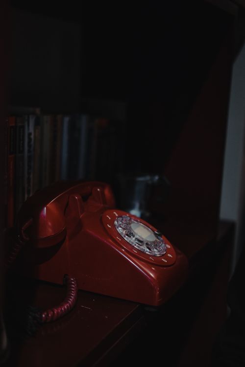Free Artistic photo of a retro red rotary phone on a wooden shelf, exuding nostalgia. Stock Photo