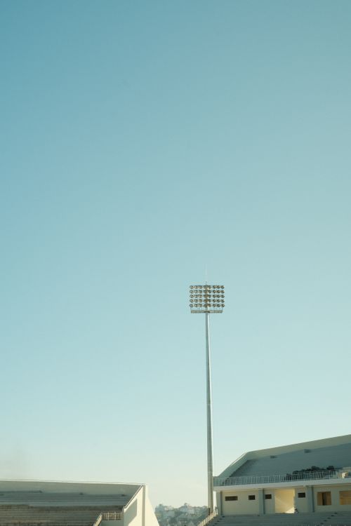 Free Minimalist outdoor stadium view with a tall floodlight under a clear blue sky. Stock Photo