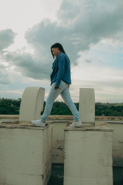 Free A stylish woman in denim poses confidently on a rooftop with a cloudy sky backdrop. Stock Photo