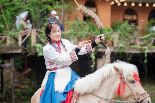 Woman wearing traditional attire on horseback, holding a bow outdoors.