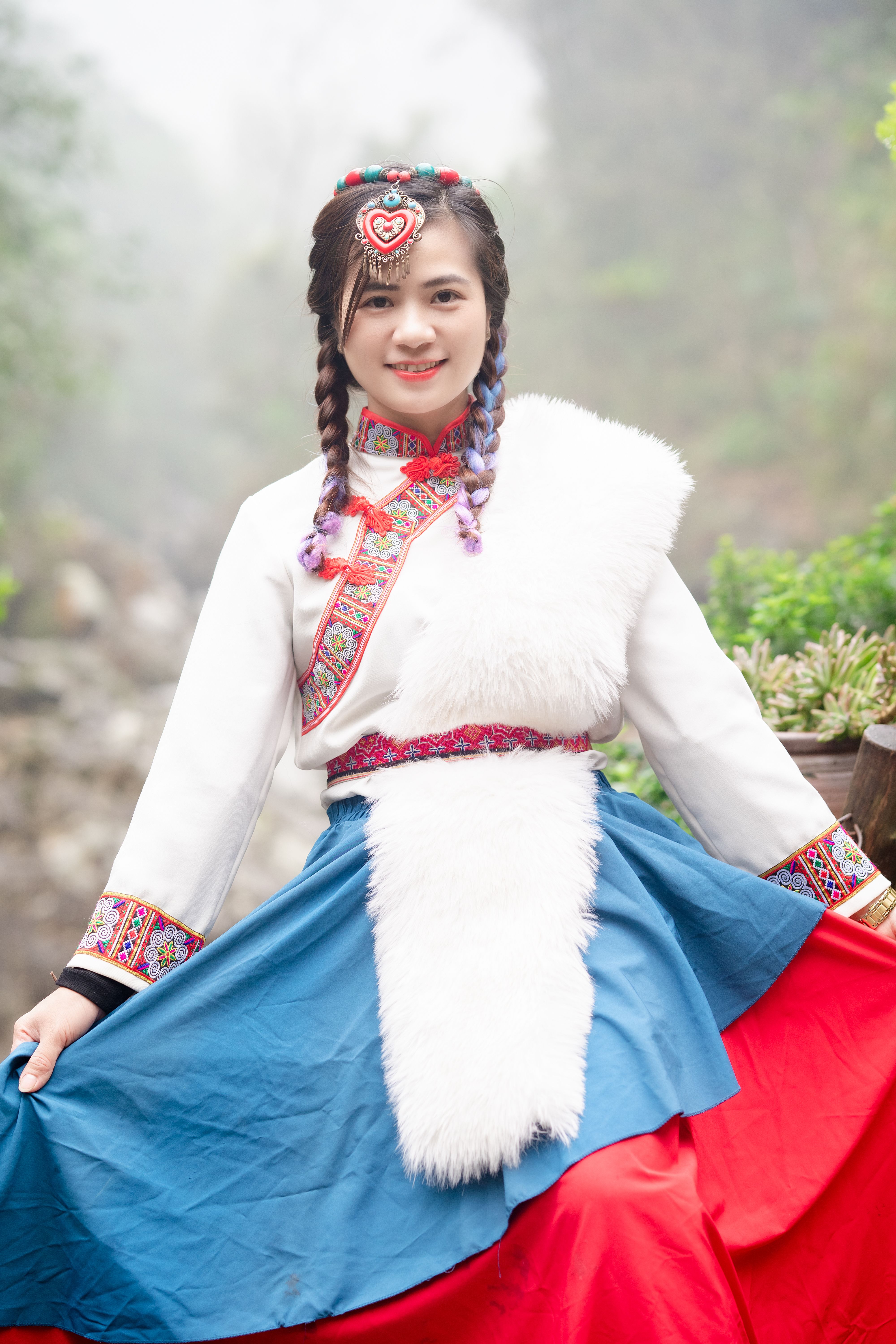 Portrait of an adult female smiling in colorful traditional attire with braided hair outdoors.