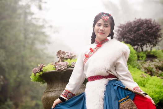 Smiling woman in traditional dress poses in a lush garden setting, showcasing cultural fashion.