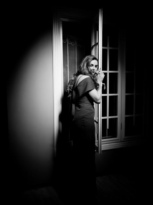 Woman in Dress Standing near Windows in Black and White