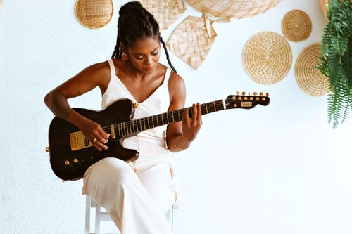 Free A young woman elegantly plays an electric guitar in a modern indoor setting. Stock Photo