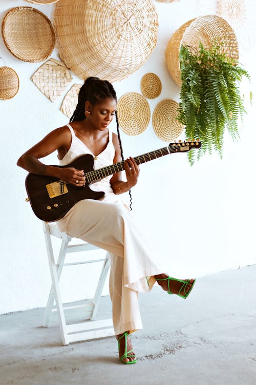 Photo of a Beautiful Young Woman Sitting and Playing an Electric Guitar
