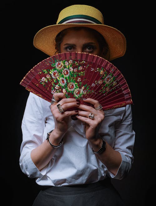 Woman in a Sun Hat Covering Her Face with a Hand Fan