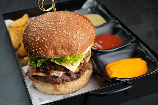 Close-up of a tasty cheeseburger with fries and sauces on a tray, ready to eat.