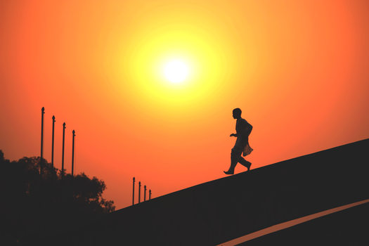 A man running against an orange sunset sky in Dhaka, Bangladesh, creating a dramatic silhouette.