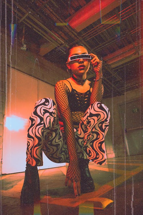 Studio Shot of a Young Woman in Patterns Pants, Futuristic Sunglasses and a Fishnet Blouse 
