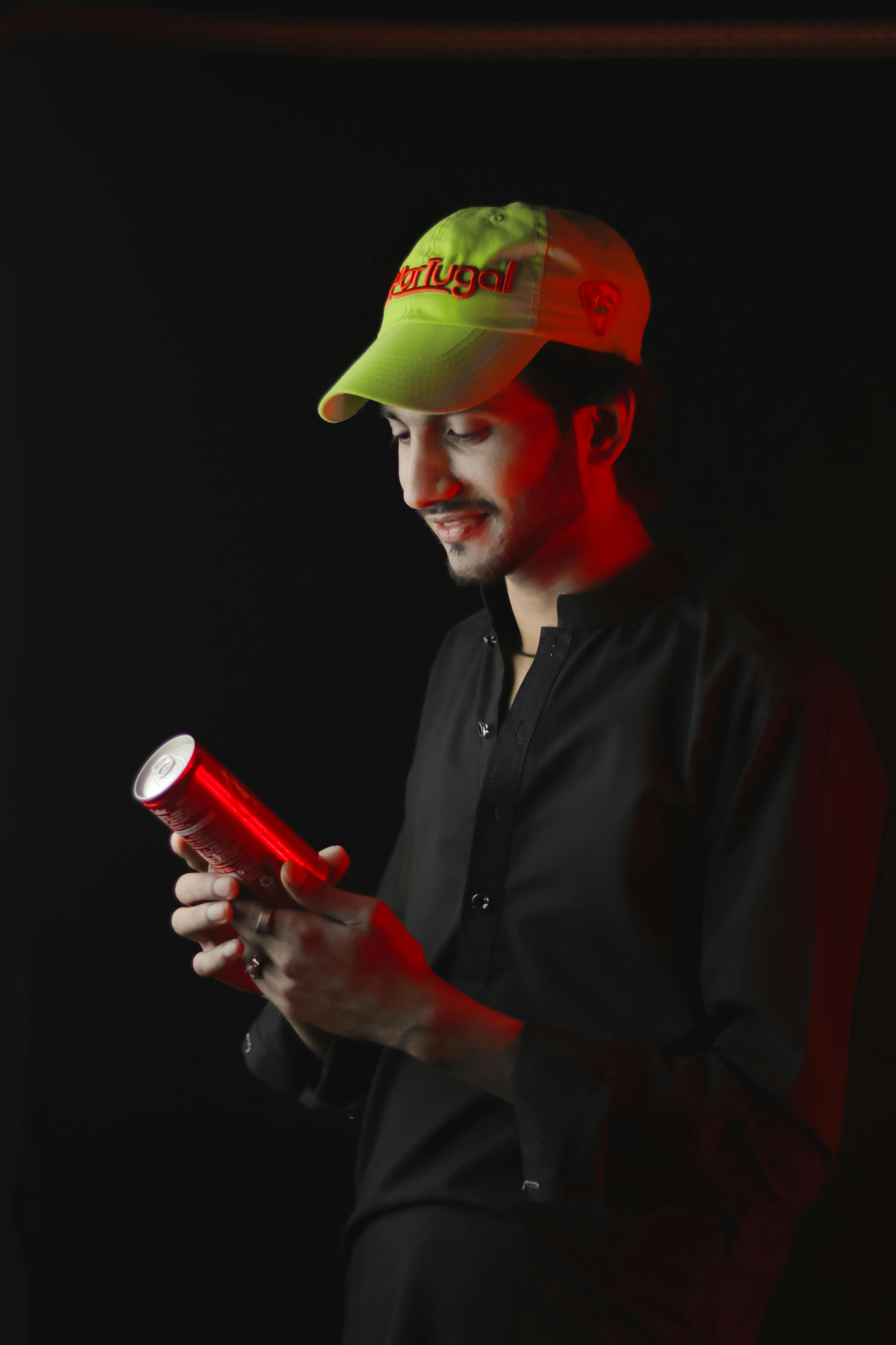 Portrait of a young man in a black shirt holding a soda can, illuminated by red light, against a dark studio background.