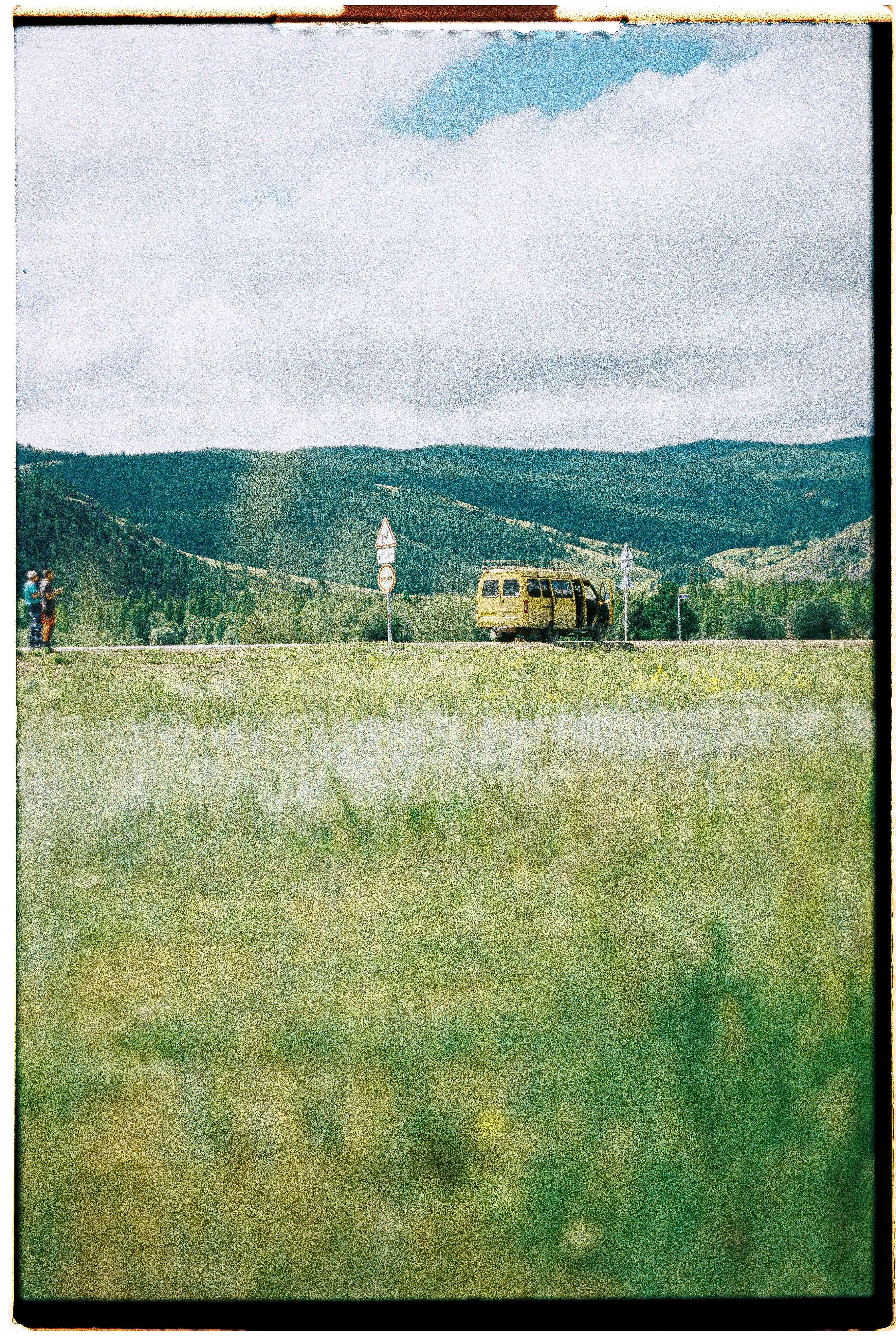 A serene countryside view featuring a yellow van on a road amidst green hills and lush grass.