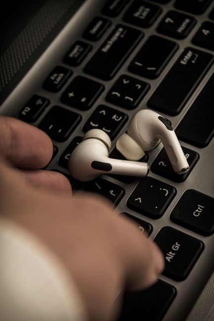 Closeup of wireless earbuds resting on a laptop keyboard, depicting modern technology.