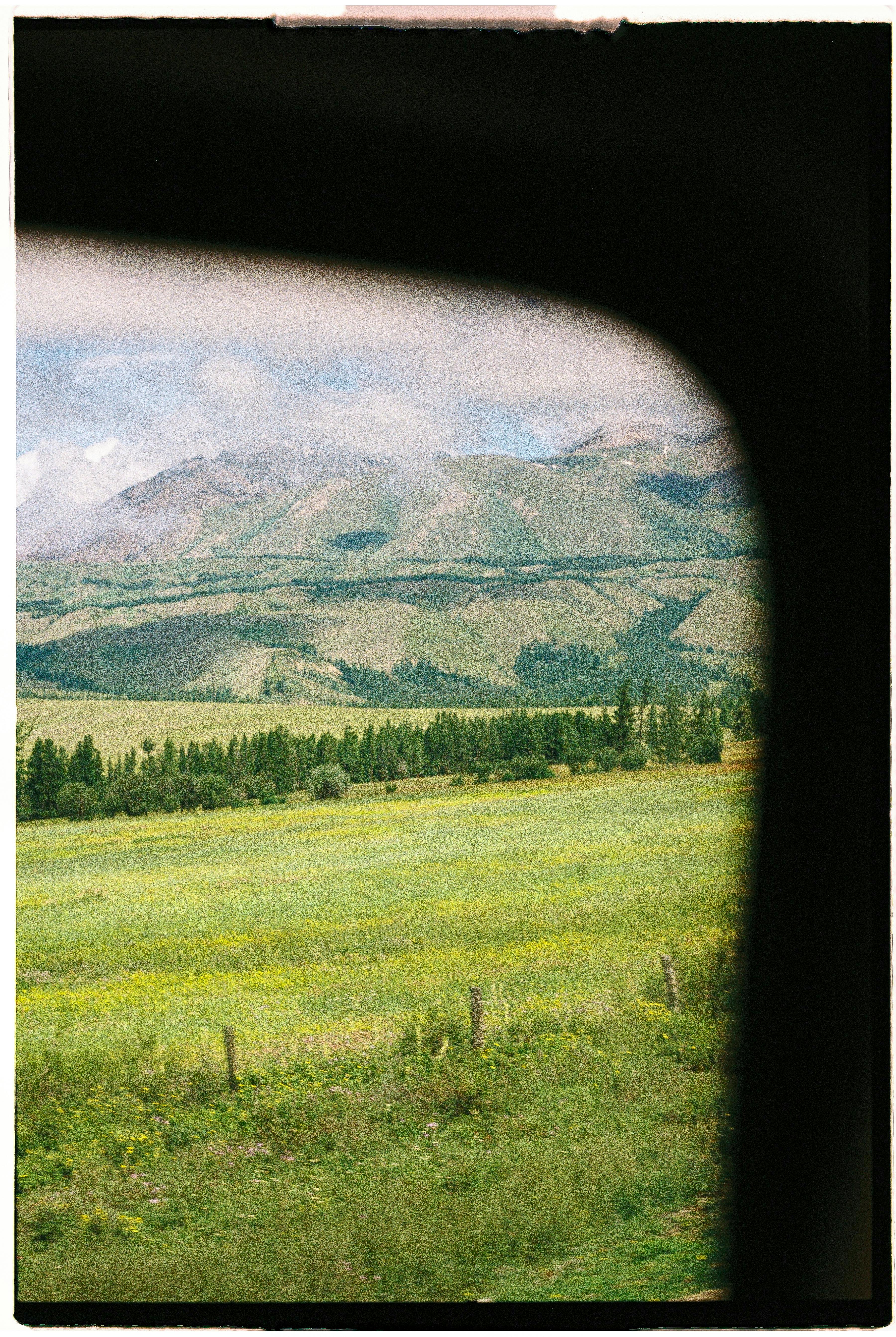Capture of rolling green hills and meadows through a window, offering a serene countryside view.