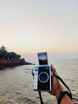 A polaroid camera held against a sunset view of the sea in Goa, India.