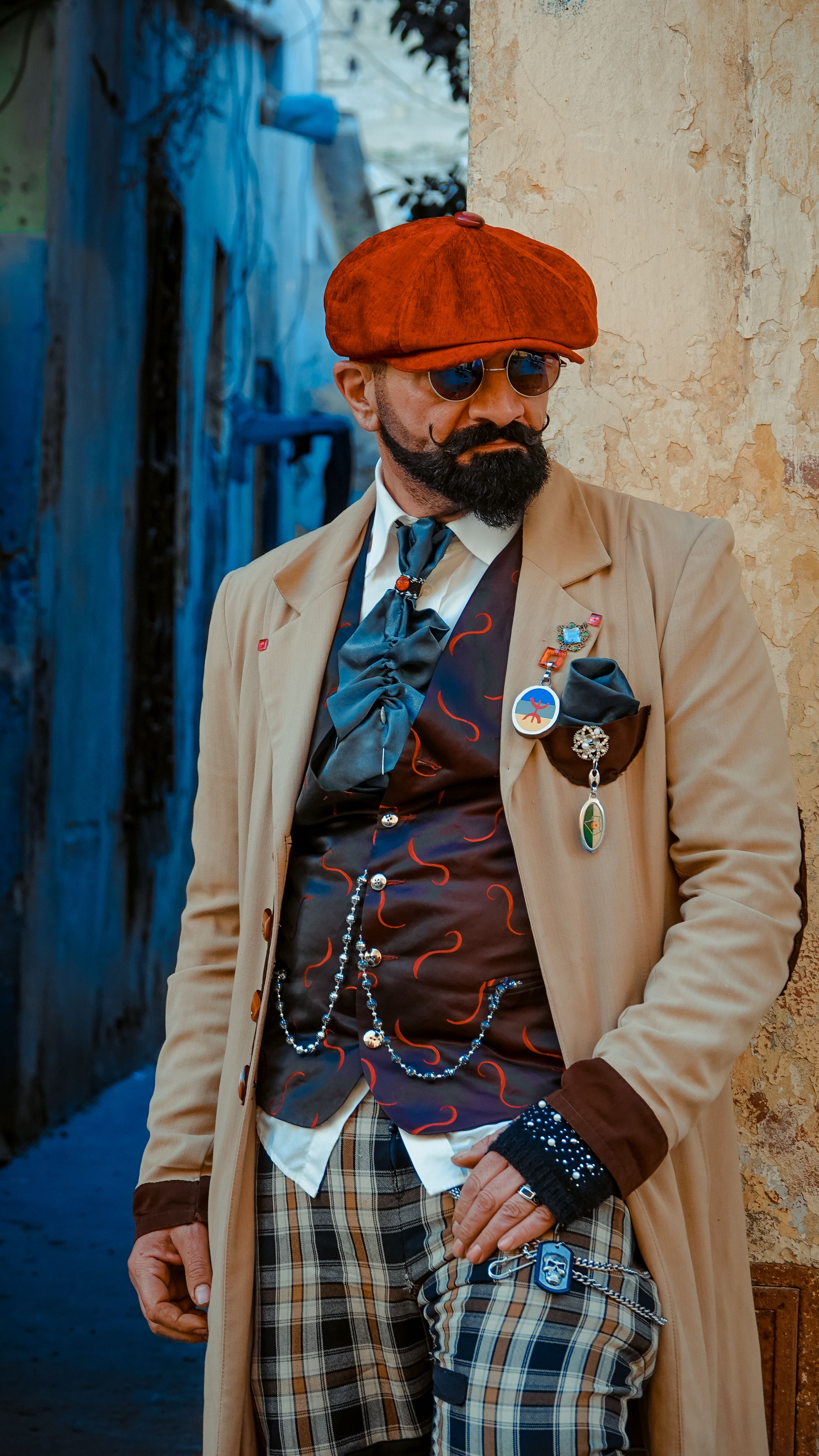 Man in vintage attire with orange hat and plaid pants posing in an alley. Vibrant colors in Oran, Algeria.