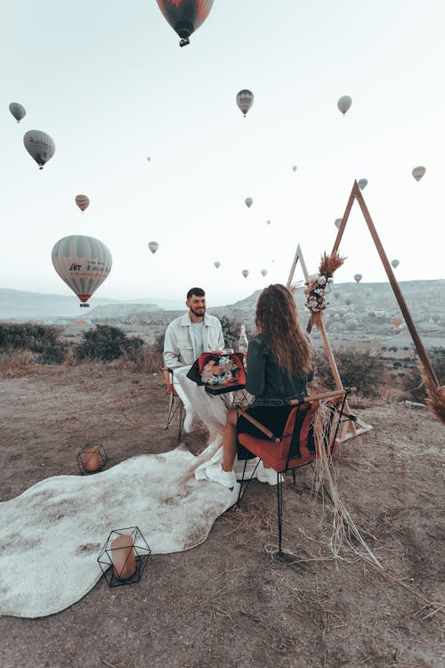 A Couple Sitting on Top of a Hill with Hot Air Balloons Flying around Them in Cappadocia, Turkey 