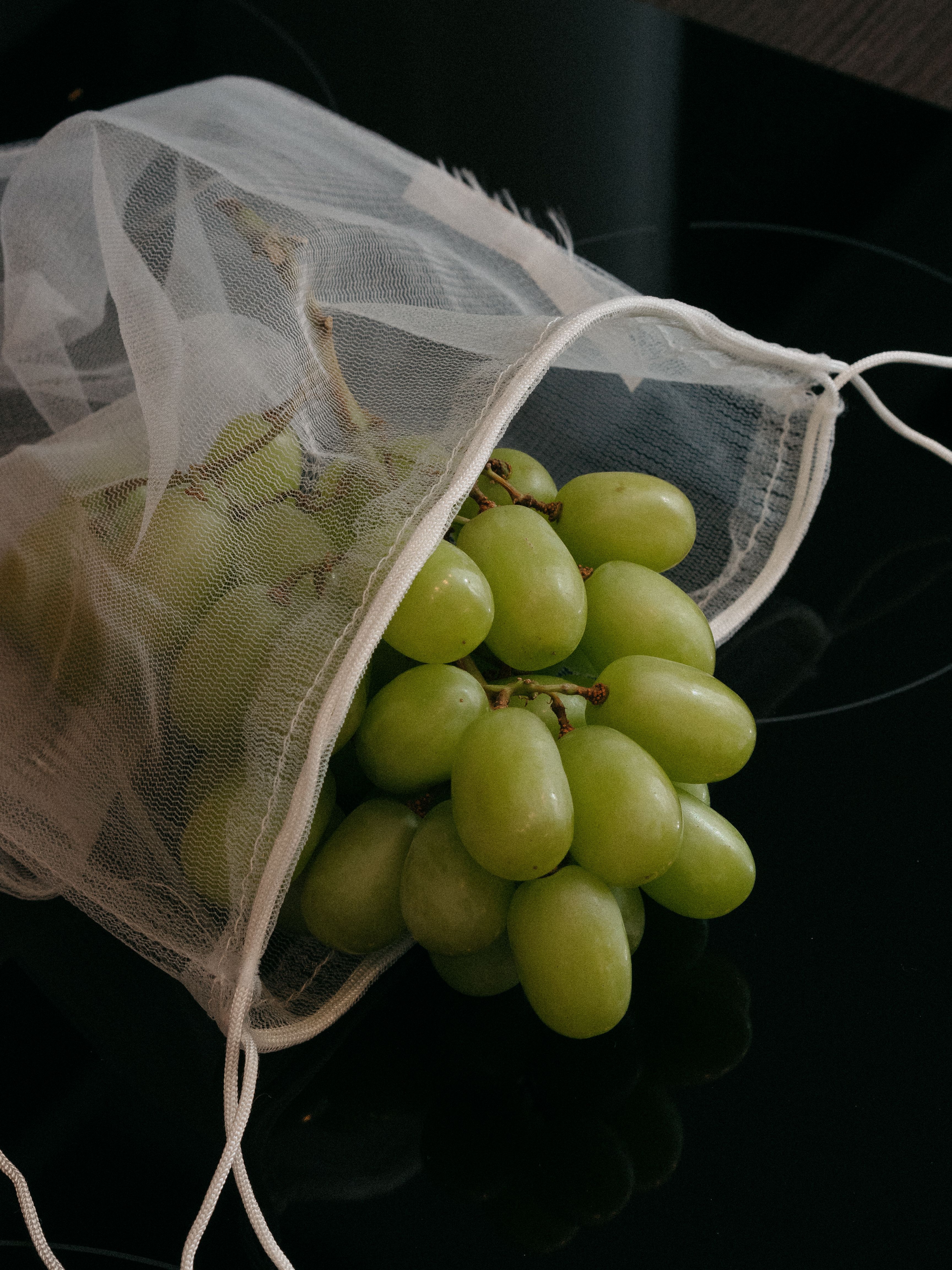 A cluster of fresh green grapes spilling from an eco-friendly mesh bag.