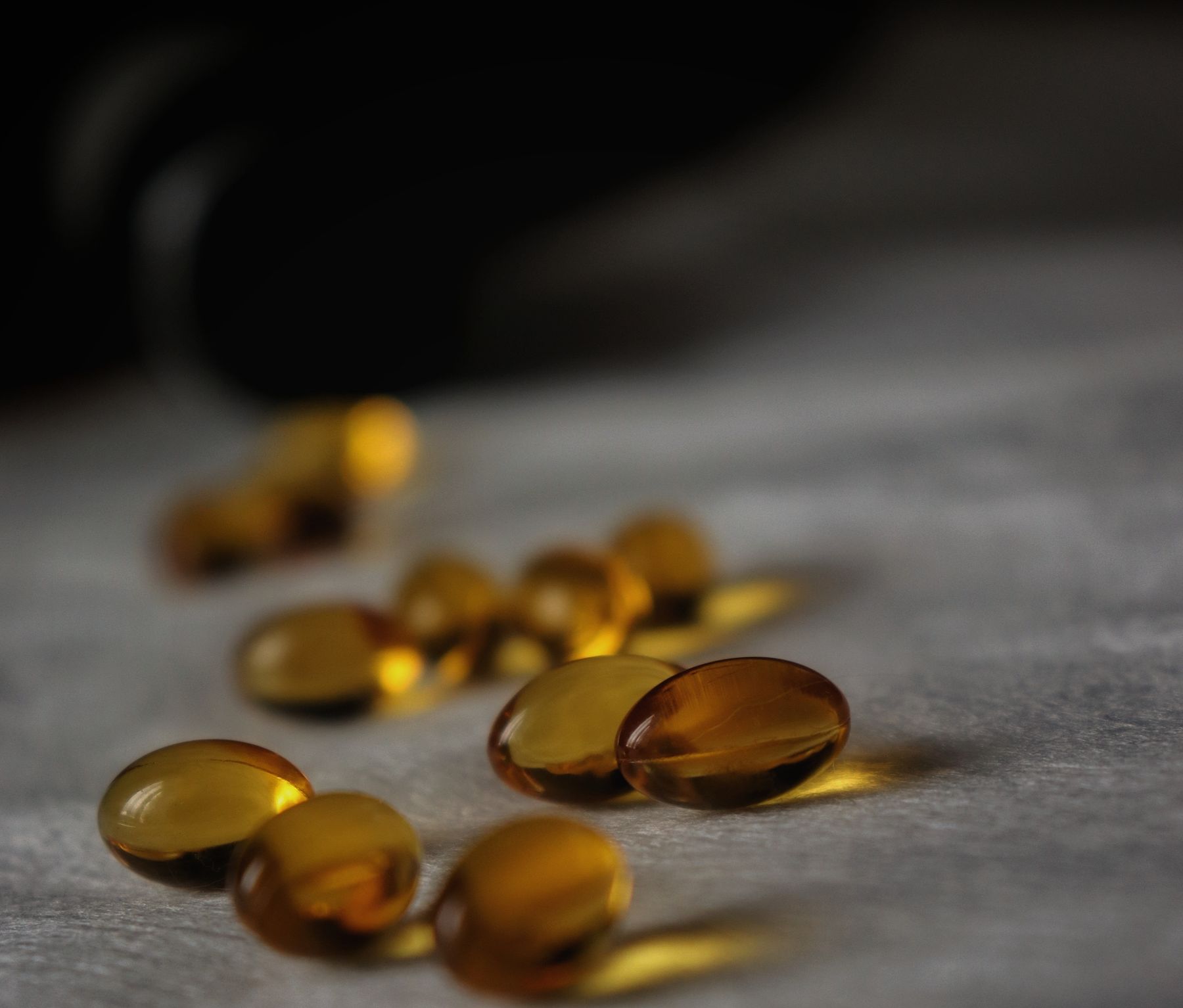 Golden softgel capsules spilling from a bottle onto a stone surface