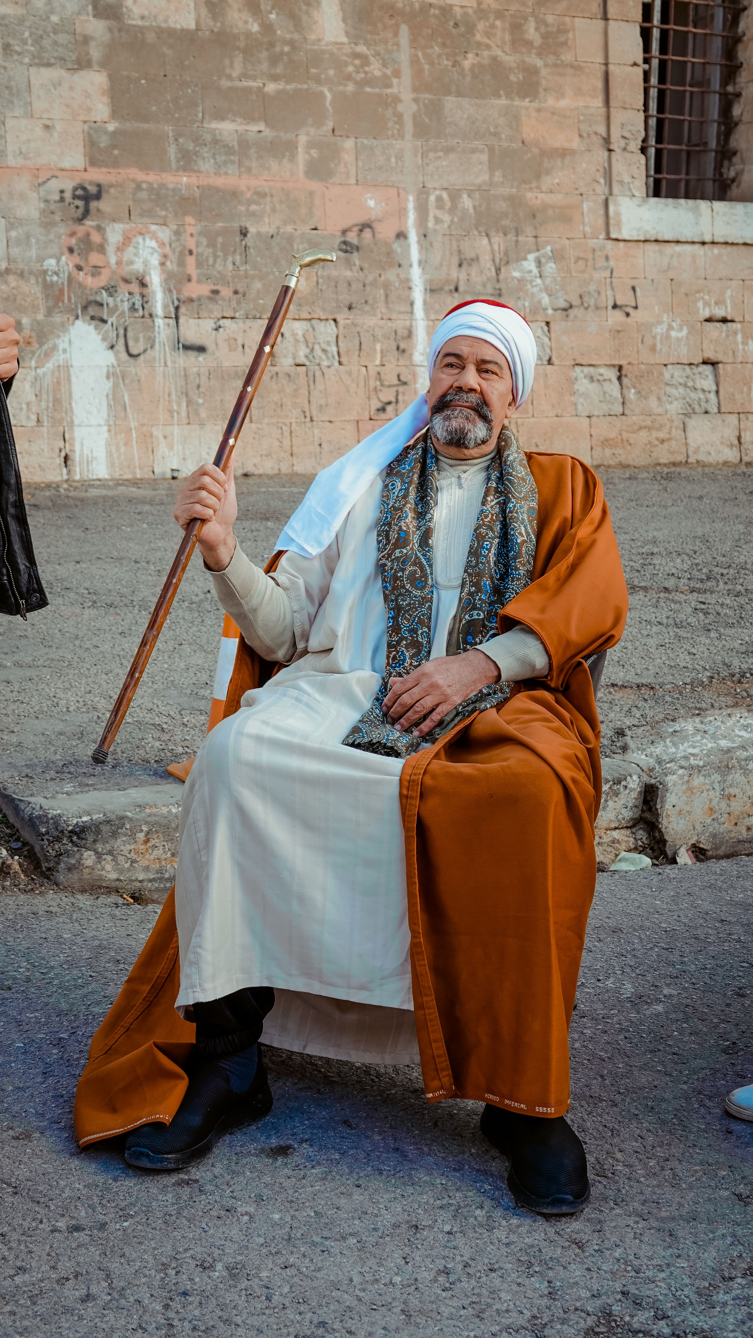Man in traditional clothing with staff sits on Alexandria street, Egypt.