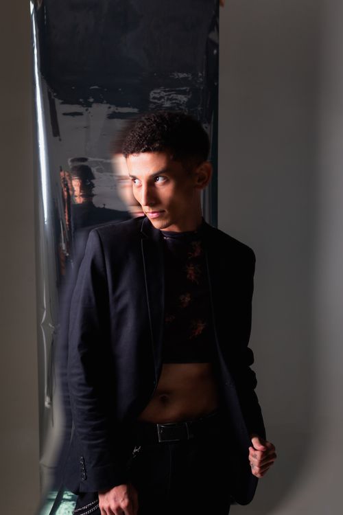 Free A model poses in a sleek black outfit against a reflective backdrop during a modern fashion shoot. Stock Photo
