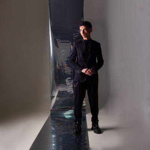 Free Stylish man in a dark suit posing in a modern studio with reflective elements. Stock Photo