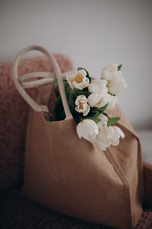 Canvas bag filled with white tulips resting on a soft pink surface.