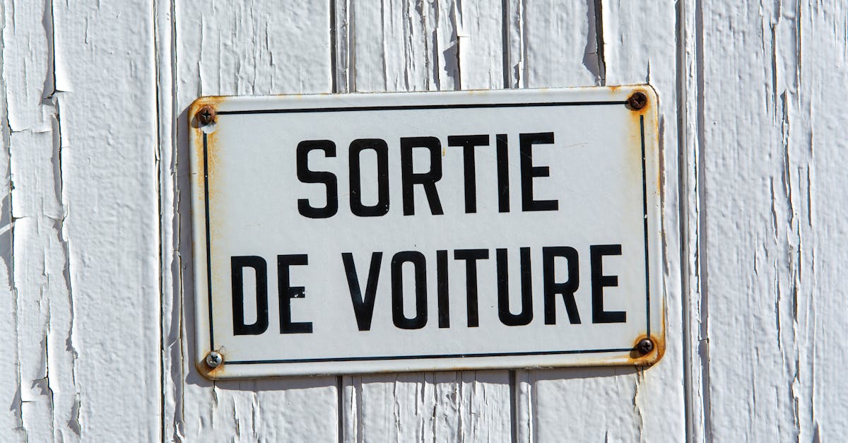 Close-up of a rustic French sign reading 'Sortie de Voiture' on a weathered white wooden wall.