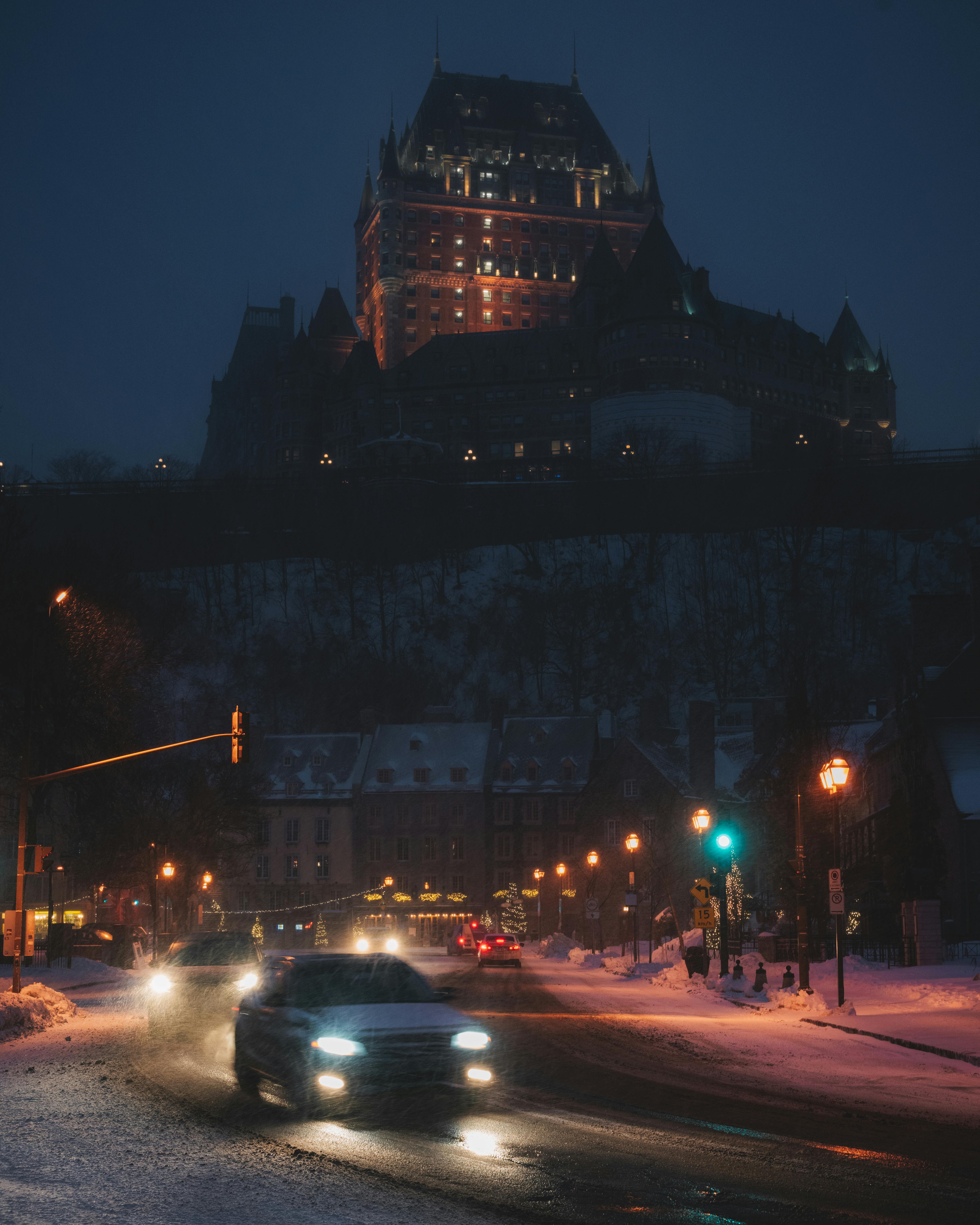 Illuminated castle with cars on a snowy city street at night, creating a moody winter scene.