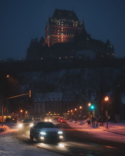 Illuminated castle with cars on a snowy city street at night, creating a moody winter scene.