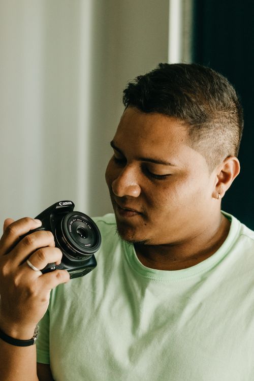 Free Close-up portrait of a young man holding and examining a camera indoors. Stock Photo