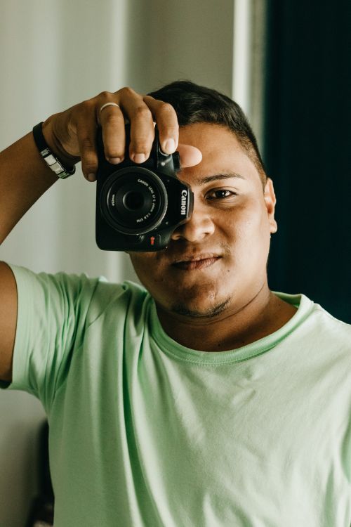 Free Man with short hair capturing self-portrait indoors using a DSLR camera. Stock Photo