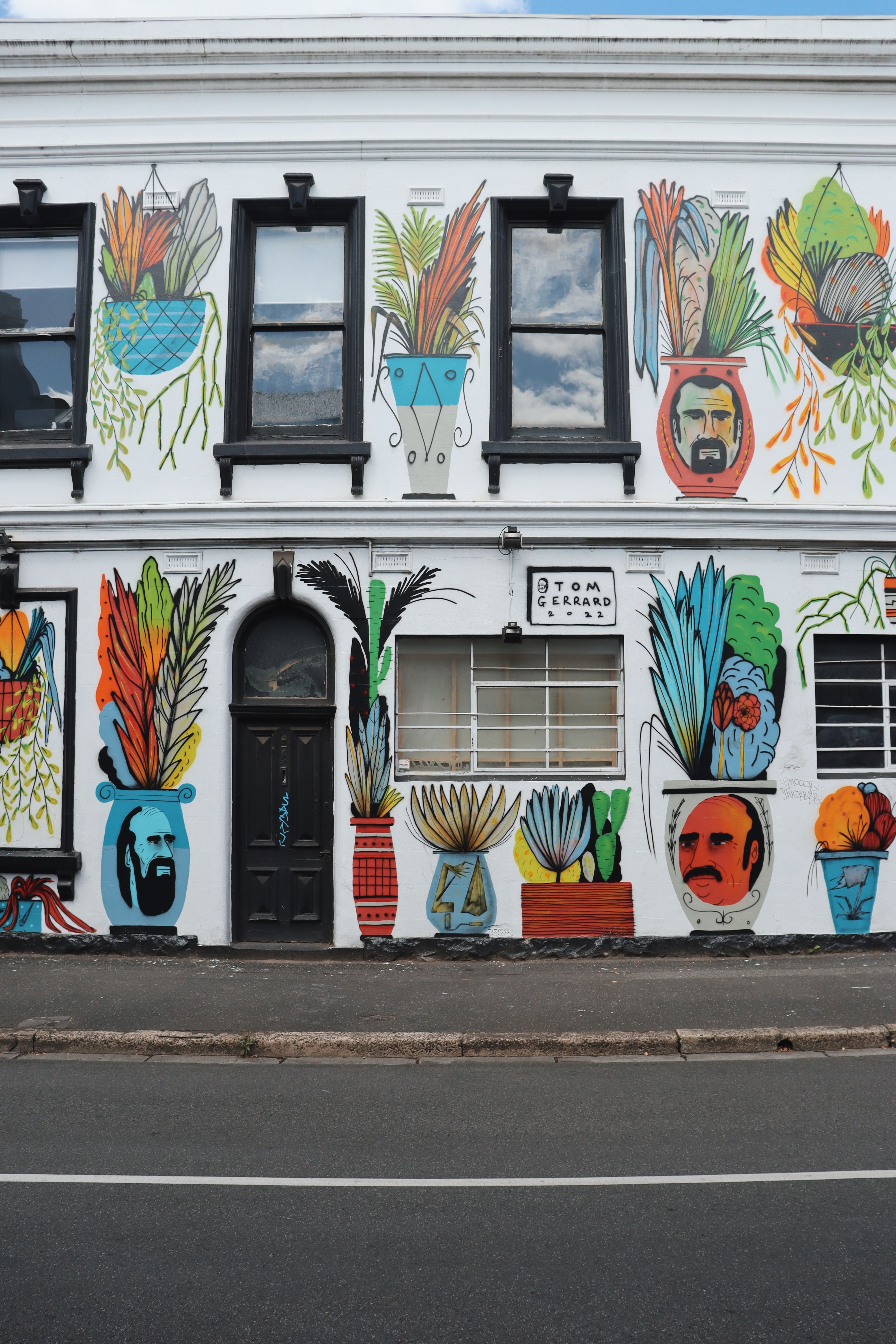 Vibrant mural featuring plant pots and faces on a building wall, urban art style.