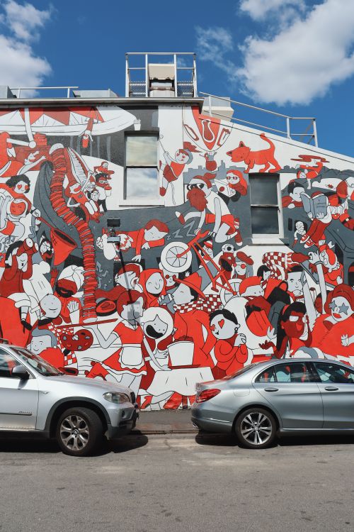 Free Colorful mural on urban building wall with parked cars under a blue sky. Stock Photo