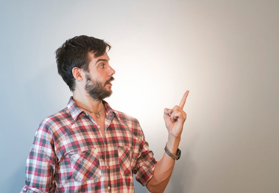 Casual bearded man in checked shirt pointing at empty space against neutral background.