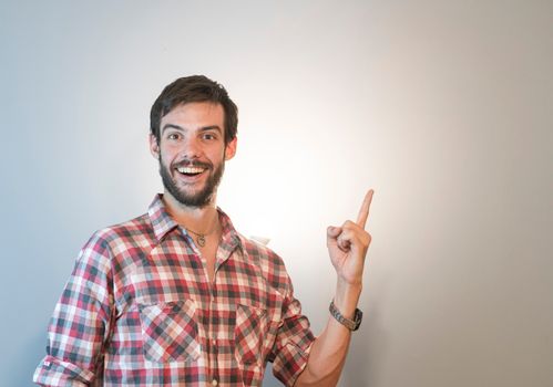 Cheerful man in plaid shirt smiles and points upwards, ideal for positive concepts.