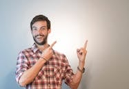 Smiling Man Pointing to an Empty Space Above His Shoulder