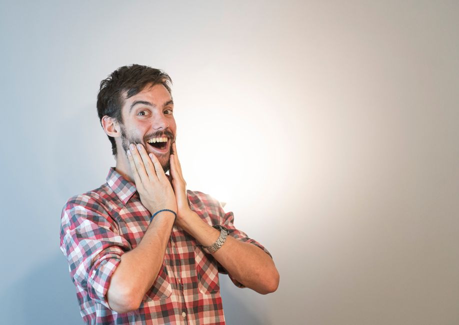 A cheerful man with a beard expressing joy with hands on cheeks and a broad smile.