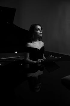 A woman in an elegant black dress sitting at a piano, embodying timeless beauty.