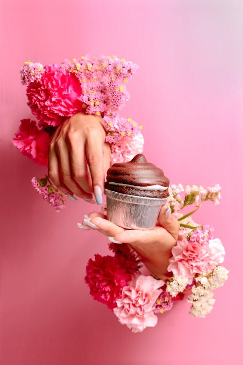 Woman Hands with Flowers around Holding Chocolate Cupcake