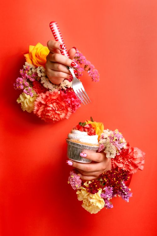 Free Colorful floral arrangement with cupcake on red background, hand holding fork adds dynamic touch. Stock Photo