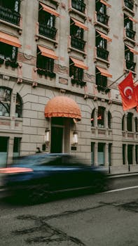 Blurred car passing a historic building with Turkish flag on a city street.