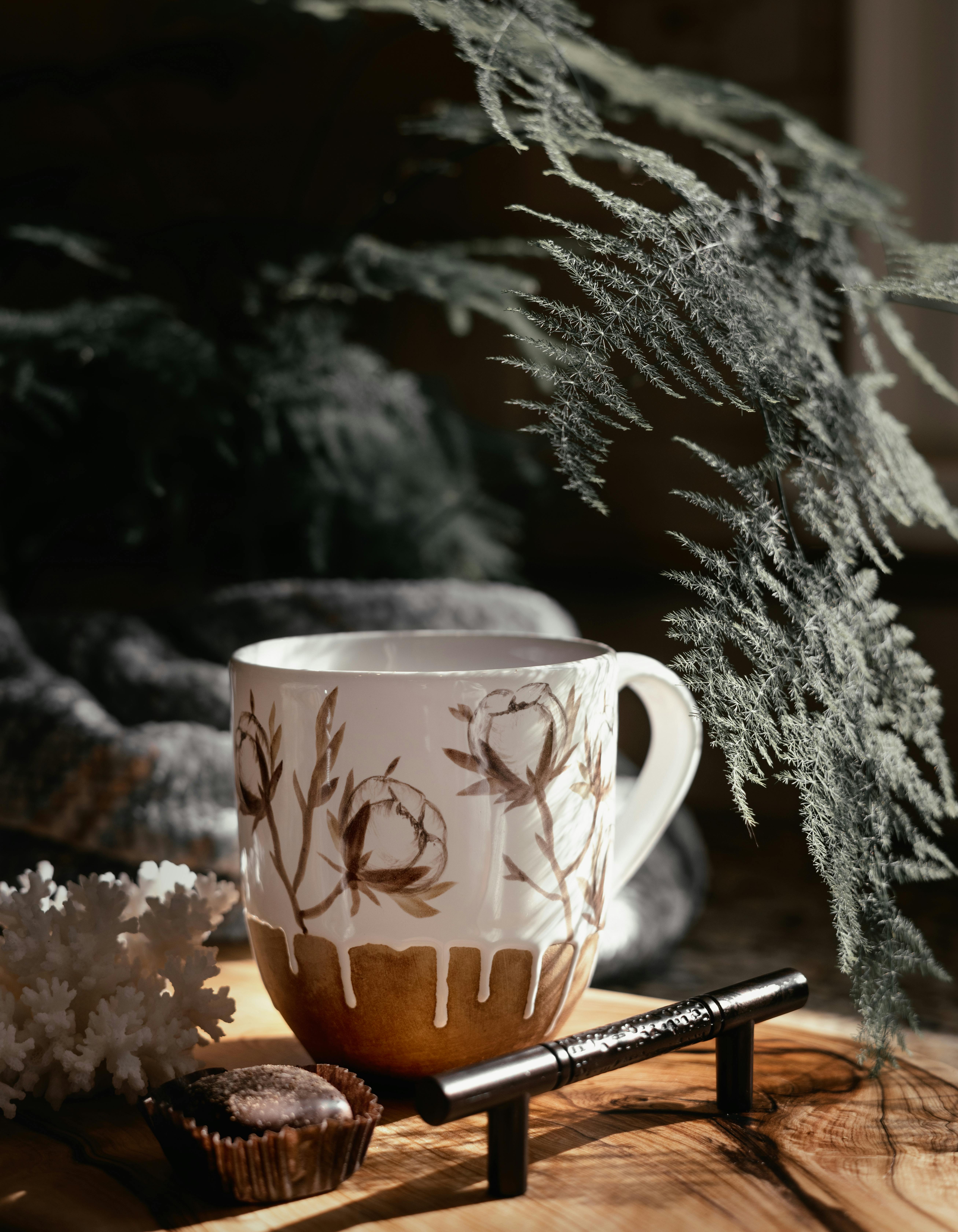 A decorative cup with leaves, surrounded by cozy elements like chocolate and foliage.