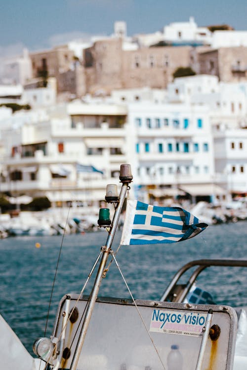 Close-up of a Small Greek Flag on a Boat and the View of Waterfront Buildings on the Shore in the Background