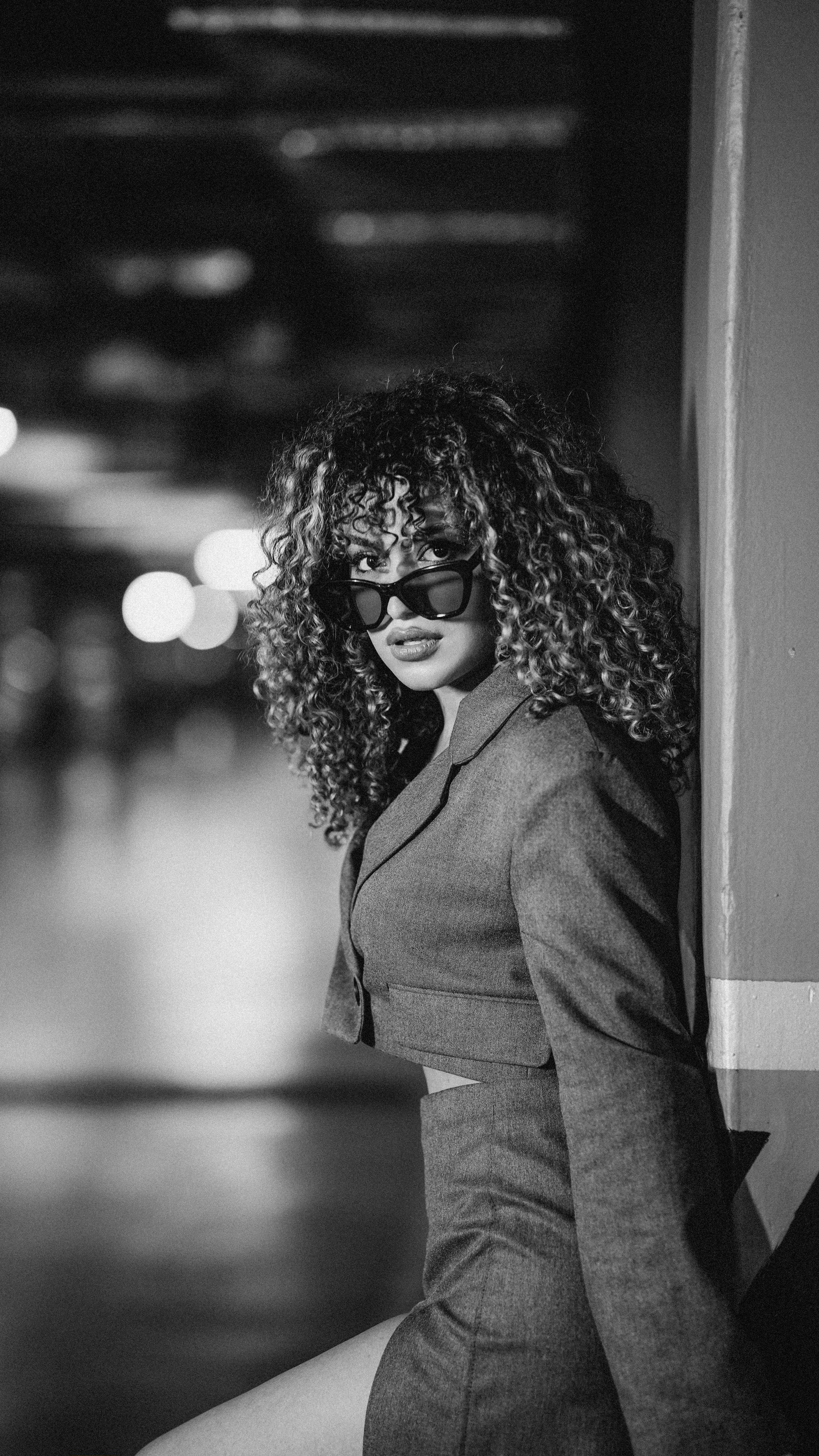 Stylish woman with curly hair in black and white portrait wearing sunglasses and jacket.