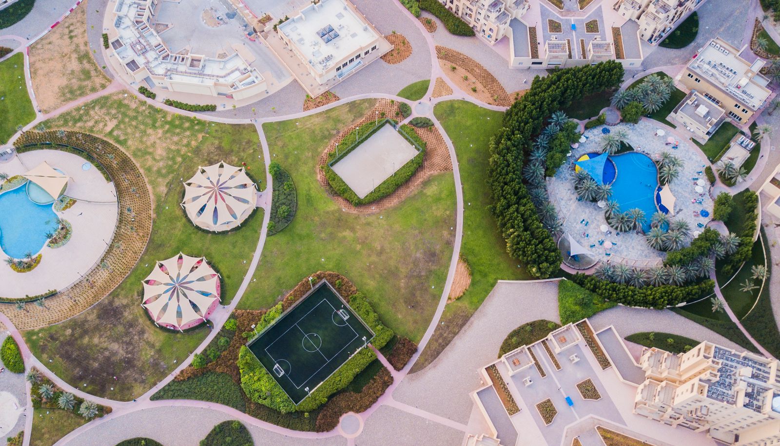 Aerial view of a landscaped community leisure park with pools and a football pitch in Dubai