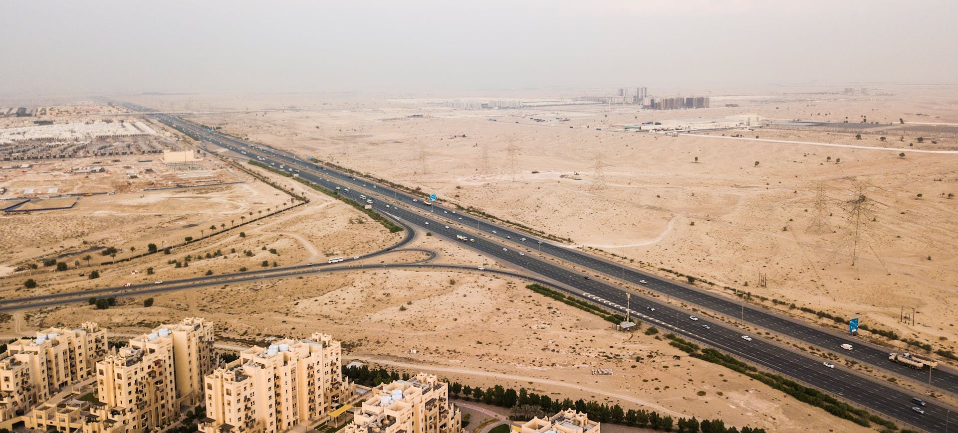 Drone shot of a highway through Dubai's desert landscape with buildings below.